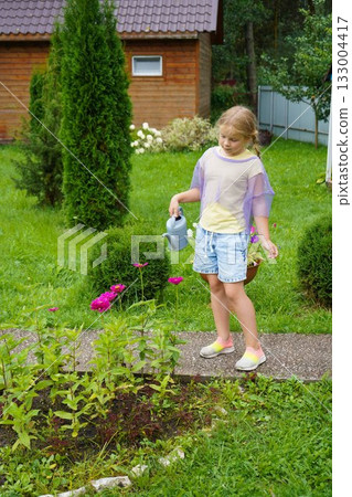 Happy young girl taking care of her garden, watering flowers with a watering can on a sunny summer day, enjoying outdoor activity and gardening Happy young girl taking care of her garden, watering flowers with a watering can on a sunny summer day, enjoying outdoor activity and gardening 133004417