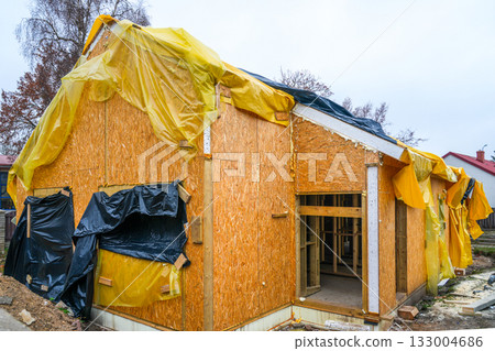 Wooden house under construction covered with plastic sheets for weather protection in autumn 133004686