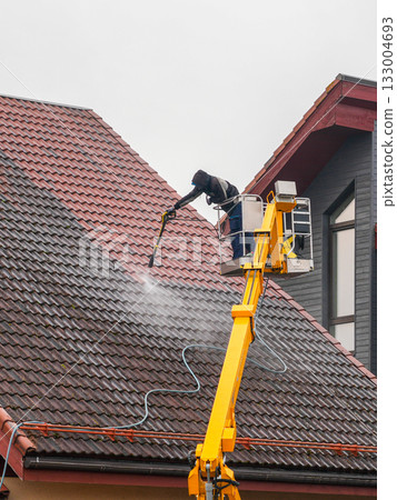 Professional worker cleaning roof tiles with high-pressure washer from yellow lift platform Professional worker cleaning roof tiles with high-pressure washer from yellow lift platform 133004693
