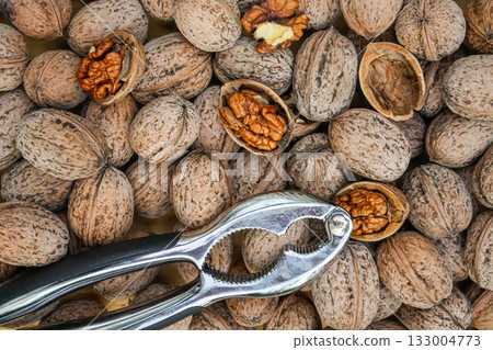 Detailed close-up of mixed open and closed walnuts with a metal nutcracker. Ideal for healthy food, farm, and nutrition themes. 133004773