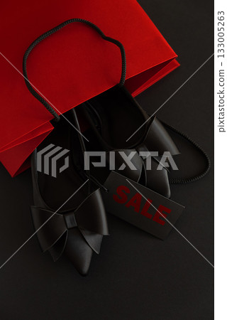 Elegant black pointed-toe shoes adorned with bows and a sale tag into red package on black background Elegant black pointed-toe shoes adorned with bows and a sale tag into red package on black background 133005263