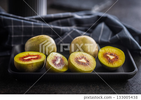 Red kiwi fruit on plate on black table. 133005438