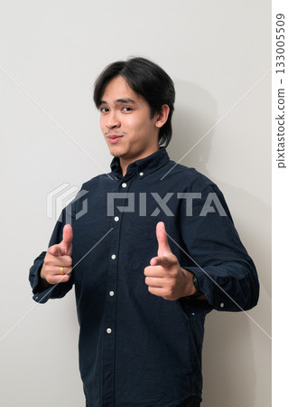 Portrait of handsome Young Asian Thai man smiling and giving thumbs up against white background Portrait of handsome Young Asian Thai man smiling and giving thumbs up against white background 133005509