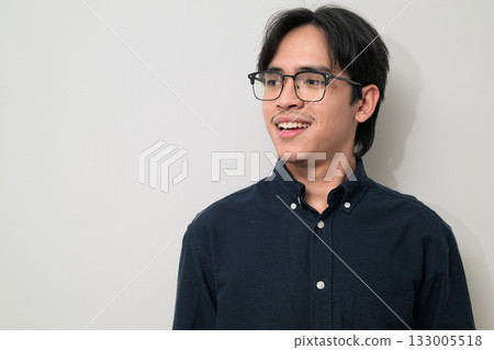 Portrait of happy young Asian Thai man wearing eyeglasses thinking against white background Portrait of happy young Asian Thai man wearing eyeglasses thinking against white background 133005518