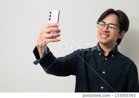 Portrait of handsome young Asian Thai man wearing eyeglasses using phone taking selfie photo 133005563