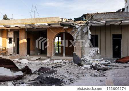 Aerial view of collapsed brick concrete building roof and facade torn away, insulation and rubble scattered across ground, archway and window frame exposed amid severe structural destruction. Aerial view of collapsed brick concrete building roof and facade torn away, insulation and rubble scattered across ground, archway and window frame exposed amid severe structural destruction. 133006274