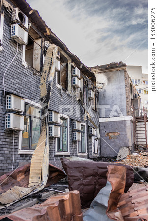 Ground level view of fire damaged building blackened brick walls broken windows twisted metal debris and intact AC units contrast with collapsed roof and scorched upper facade. 133006275