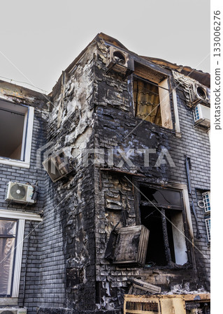 Ground level view of fire ravaged brick building blackened walls, melted AC units, shattered windows, and exposed interior reveal extensive heat damage and structural vulnerability. Ground level view of fire ravaged brick building blackened walls, melted AC units, shattered windows, and exposed interior reveal extensive heat damage and structural vulnerability. 133006276