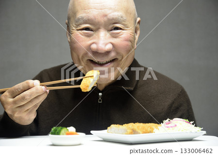 一位老人面帶微笑地吃著炸豬排。 133006462