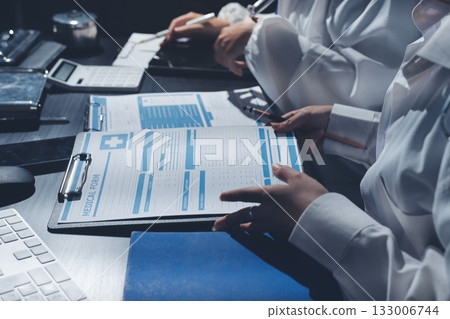 Two doctors and a female nurse meet at a table in the hospital, collaborating on medical tasks using laptops and computers 133006744
