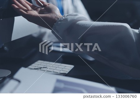 Two doctors and a female nurse meet at a table in the hospital, collaborating on medical tasks using laptops and computers 133006760