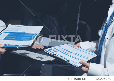 Two doctors and a female nurse meet at a table in the hospital, collaborating on medical tasks using laptops and computers 133006770