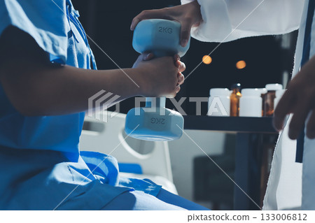 Physical therapist assisting a woman with dumbbell exercise 133006812