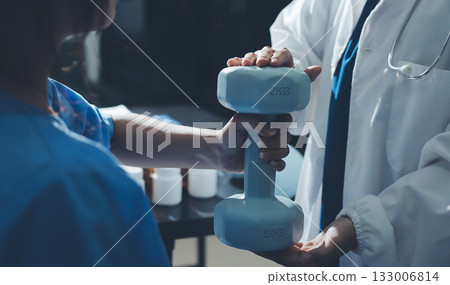 Physical therapist assisting a woman with dumbbell exercise 133006814