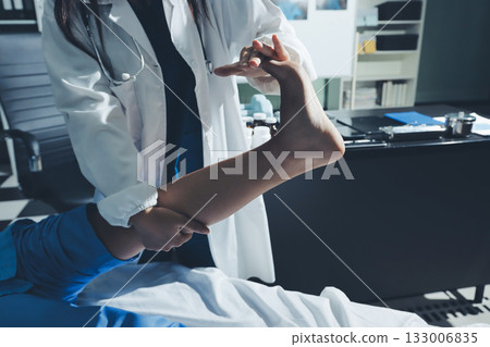 Doctor examining and supporting injured ankle of female patient in hospital room, providing medical assistance and treatment for sprain or fracture Doctor examining and supporting injured ankle of female patient in hospital room, providing medical assistance and treatment for sprain or fracture 133006835