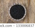 Nigela sativa black cumin in a crystal bowl on a beige wooden table. 133006837