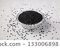 Black cumin (Nigella sativa) in a crystal bowl scattered on a grey concrete table. 133006898