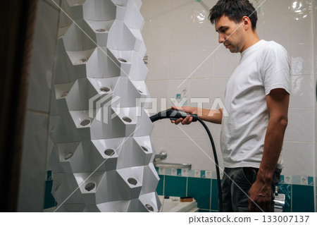 Male using steam cleaner to sanitize vertical hydroponic tower garden in bathroom, demonstrating modern and sustainable approach to indoor gardening and hygiene. Concept of home gardening. Male using steam cleaner to sanitize vertical hydroponic tower garden in bathroom, demonstrating modern and sustainable approach to indoor gardening and hygiene. Concept of home gardening. 133007137