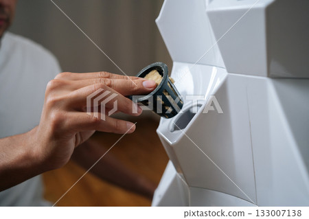 Close-up of male hands placing rockwool cube inside net pot, inserting it into hydroponic tower system, preparing for seed starting and modern agriculture. Concept of home gardening. Close-up of male hands placing rockwool cube inside net pot, inserting it into hydroponic tower system, preparing for seed starting and modern agriculture. Concept of home gardening. 133007138