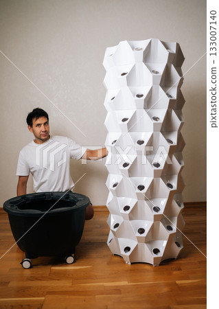 Vertical portrait of urban farmer assembling vertical hydroponic tower, growing fresh produce in compact indoor space with sustainable agricultural technology. Concept of home gardening. Vertical portrait of urban farmer assembling vertical hydroponic tower, growing fresh produce in compact indoor space with sustainable agricultural technology. Concept of home gardening. 133007140