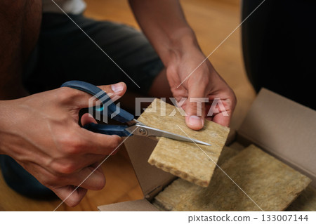 Close-up hands of unrecognizable gardener cutting piece of rockwool with scissors, preparing it for seed starting in hydroponic system. Concept of healthy and sustainable cultivation. 133007144