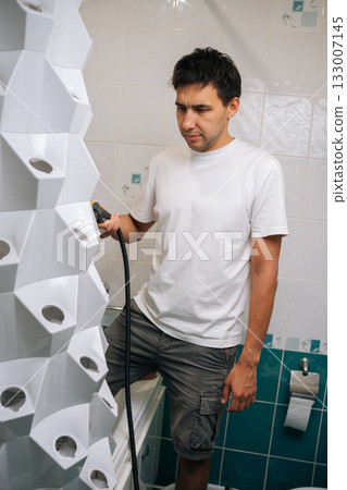 Vertical portrait of gardener sanitizing vertical hydroponic tower garden with steam cleaner in bathroom, highlighting innovative indoor gardening and cleaning technique. Concept of home gardening. Vertical portrait of gardener sanitizing vertical hydroponic tower garden with steam cleaner in bathroom, highlighting innovative indoor gardening and cleaning technique. Concept of home gardening. 133007145