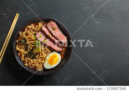 Ramen soup with beef, egg, seaweed and chopsticks on dark background top view, space for text 133007168