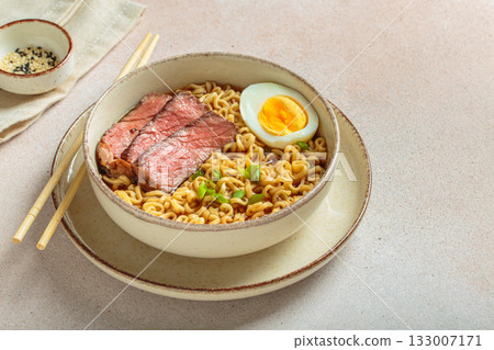 Ramen or asian style noodles soup with beef, egg and green onions in bowl on light beige background 133007171