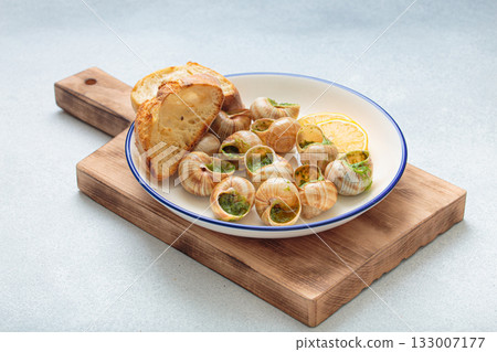 Escargots de bourgogne snails with garlic butter, parsley and lemon wedges on white plate on light background 133007177