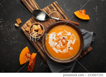 Pumpkin soup croutons cream fresh pumpkin slices wooden board dark background autumn winter 133007191