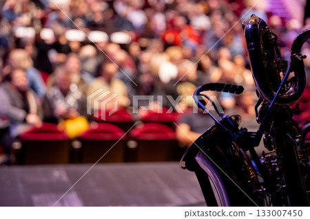 A saxophone shines on stage while an enthusiastic audience enjoys the performance in the background 133007450