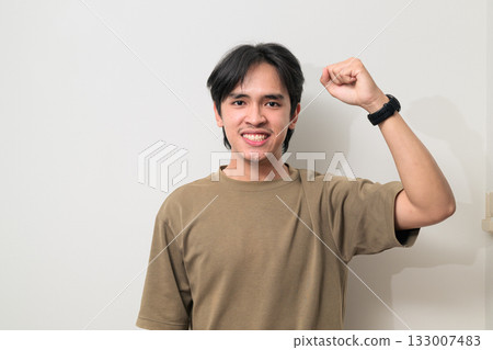 Portrait of happy young Asian Thai man with arm raised smiling against white background Portrait of happy young Asian Thai man with arm raised smiling against white background 133007483