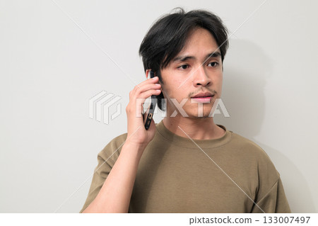 Portrait of handsome young Asian Thai man talking on the phone against white background Portrait of handsome young Asian Thai man talking on the phone against white background 133007497