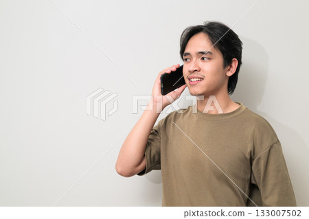 Portrait of happy young Asian Thai man talking on the phone against white background 133007502