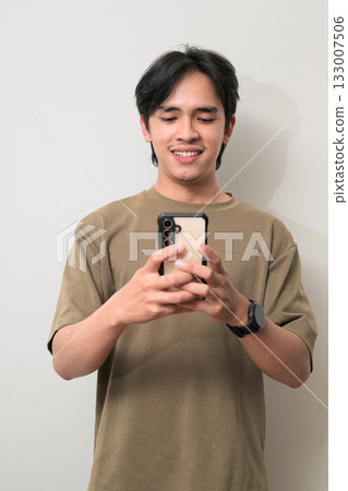 Portrait of handsome young Asian Thai man using phone texting against white background Portrait of handsome young Asian Thai man using phone texting against white background 133007506