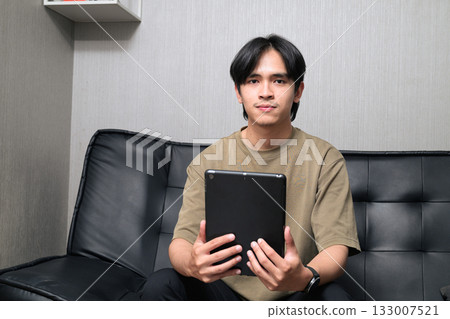 Portrait of handsome Young Asian Thai man using digital tablet computer at home Portrait of handsome Young Asian Thai man using digital tablet computer at home 133007521