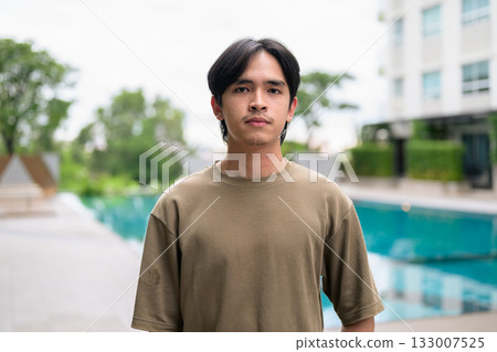 Portrait of handsome Young Asian Thai man outdoors next to swimming pool during summer Portrait of handsome Young Asian Thai man outdoors next to swimming pool during summer 133007525