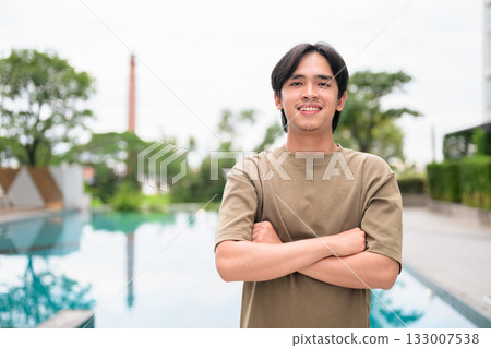 Portrait of handsome Young Asian Thai man outdoors next to swimming pool during summer Portrait of handsome Young Asian Thai man outdoors next to swimming pool during summer 133007538