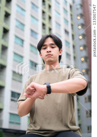 Portrait of handsome Young Asian Thai man using smartwatch outdoors low angle view 133007547