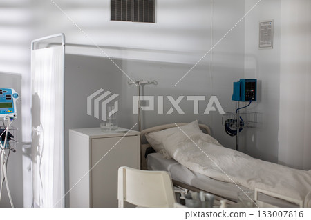 A hospital room furnished with an empty bed and various essential medical equipment present A hospital room furnished with an empty bed and various essential medical equipment present 133007816