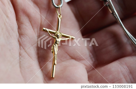 Gold cross pendant held in a hand with close up view 133008191