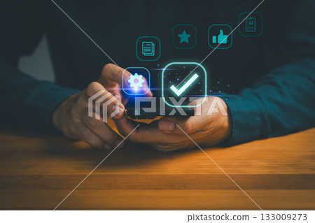 Person holding smartphone with digital icons of settings, checkmark, star, like, and documents, symbolizing mobile app approval, user satisfaction, quality assurance and digital technology management. Person holding smartphone with digital icons of settings, checkmark, star, like, and documents, symbolizing mobile app approval, user satisfaction, quality assurance and digital technology management. 133009273