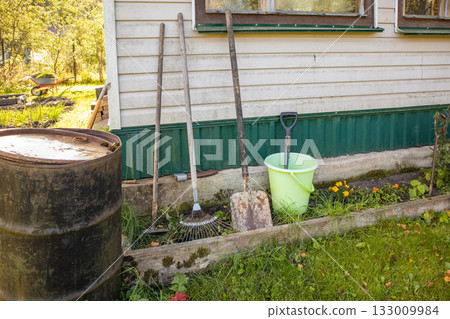 Garden tools by house wall country yard with green bucket 133009984