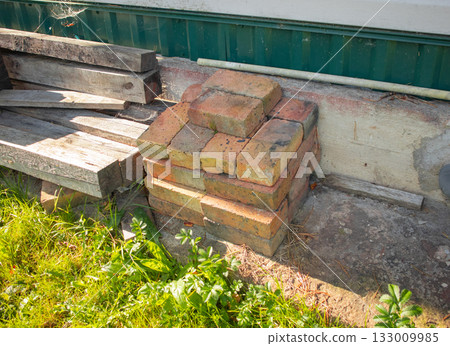Stack of old bricks and wooden planks by house wall backyard materials 133009985