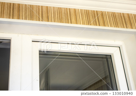 White PVC window frame and striped wallpaper with crown molding close up 133010940
