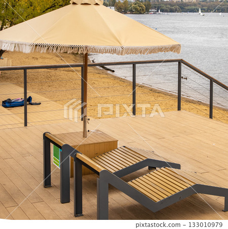 Wooden sun loungers and beige umbrella on deck urban beach vertical frame Wooden sun loungers and beige umbrella on deck urban beach vertical frame 133010979