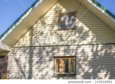 House facade with beige siding and wooden windows sunny shadows 133010993