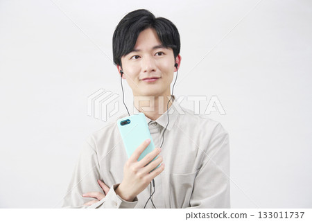 A man in his 20s listening to music with earphones on a white background 133011737