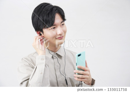 一位 20 多歲的男子戴著耳機在白色背景上聽音樂 133011738