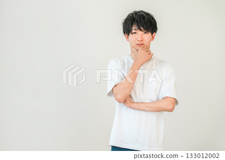 A young Asian man resting his chin on his hand (thinking, considering, worrying, choosing, troubled, worried) A young Asian man resting his chin on his hand (thinking, considering, worrying, choosing, troubled, worried) 133012002
